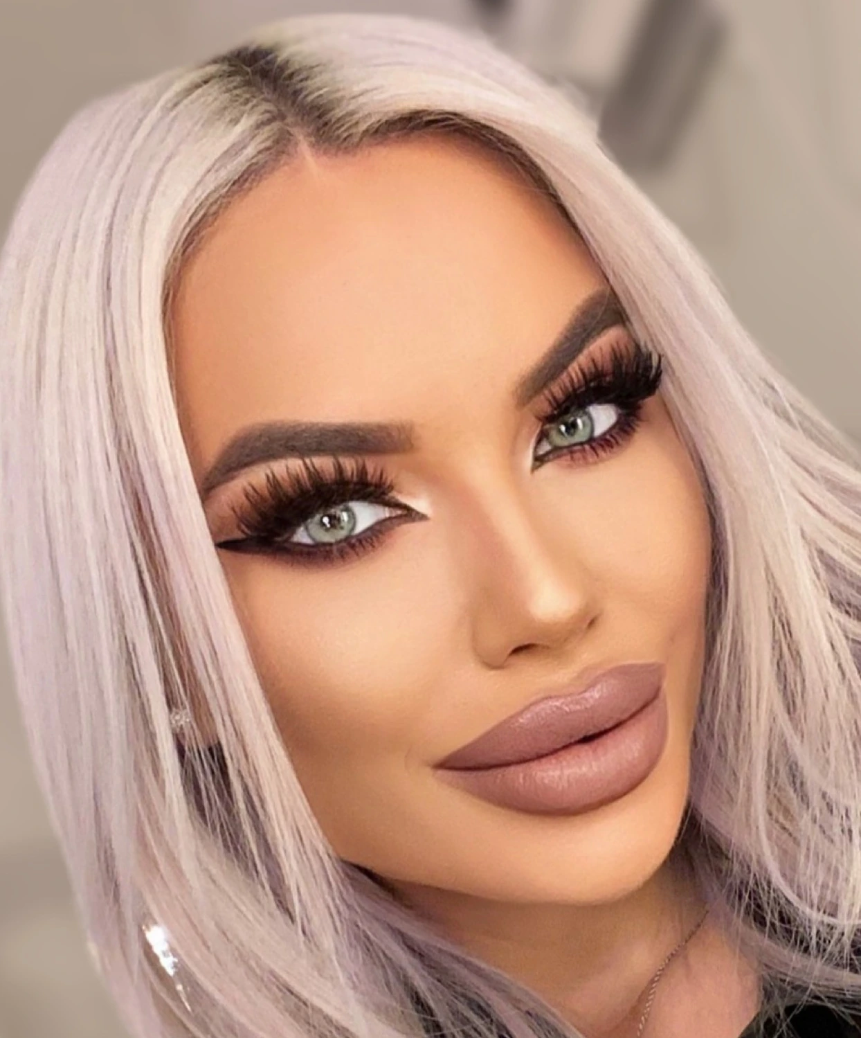 Sasha in a close-up: platinum hair, pale green eyes, full wispy lashes over a black wing, brushed brows, sculpted cheekbones and a glossy nude lip.