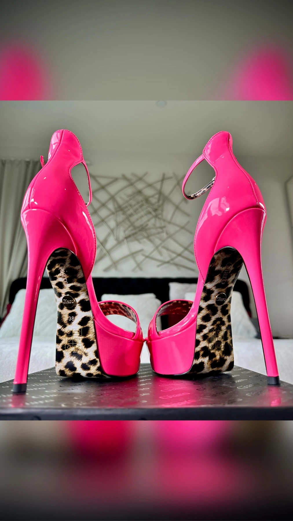A pair of hot pink patent platform stilettos seen from behind, their soles in leopard print.