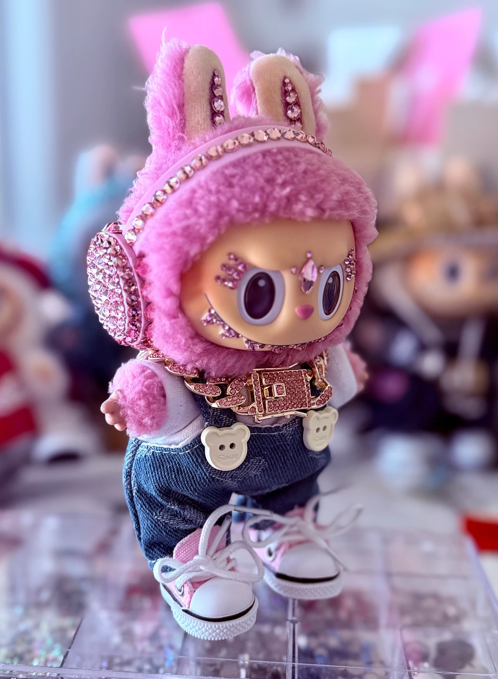 Labubu Nº 01: pink fluffy hood, crystal ear muffs, a jewelled belt, denim overalls and white sneakers.