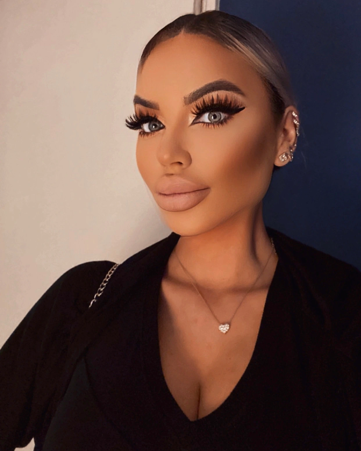 Sasha with her hair in a sleek bun: winged liner, soft bronze glam and a small diamond heart pendant.