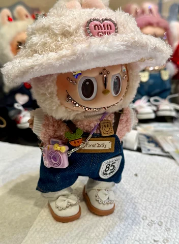 Labubu Nº 02: cream fluffy bucket hat, a little pink camera bag and denim overalls with an 85 patch.