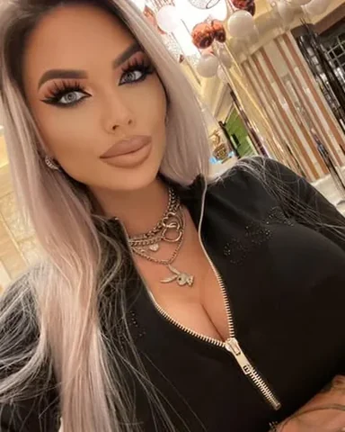 Sasha with long blonde waves in a black zip top, close up.